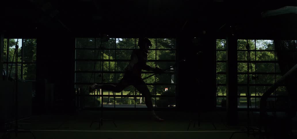 A lacrosse player jumps to shoot and runs across an indoor field in slow motion with dramatic strobe lighting