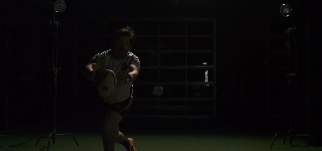 A rugby player throws a pass in dramatic slow motion under bright studio lights