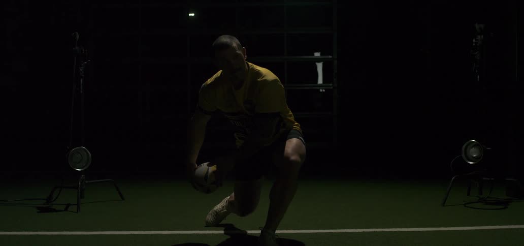 A strong rugby player in a studio setting passes the ball in super slow motion with dramatic lighting effects