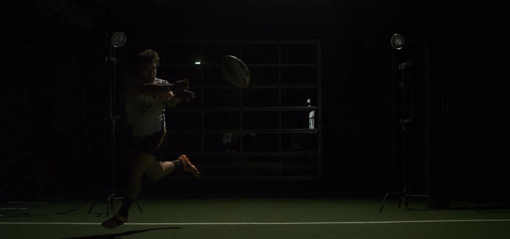Dramatic slow-motion shot of a rugby player passing the ball in a dark, spotlit indoor arena