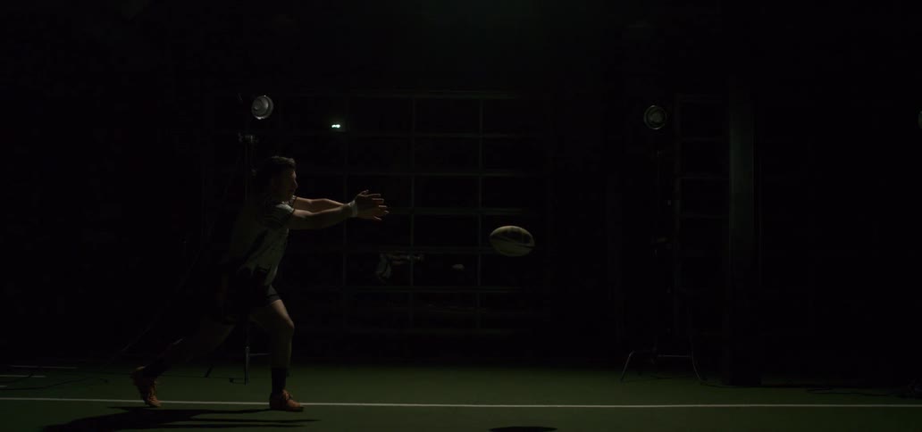 A female rugby player passes a rugby ball in slow motion with dramatic strobe lighting effects in an indoor training facility