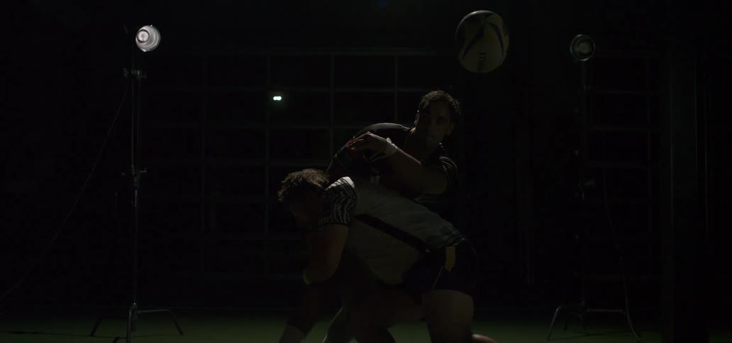 Two rugby players collide in a powerful tackle, captured in dramatic super slow motion with a cinematic flash of light