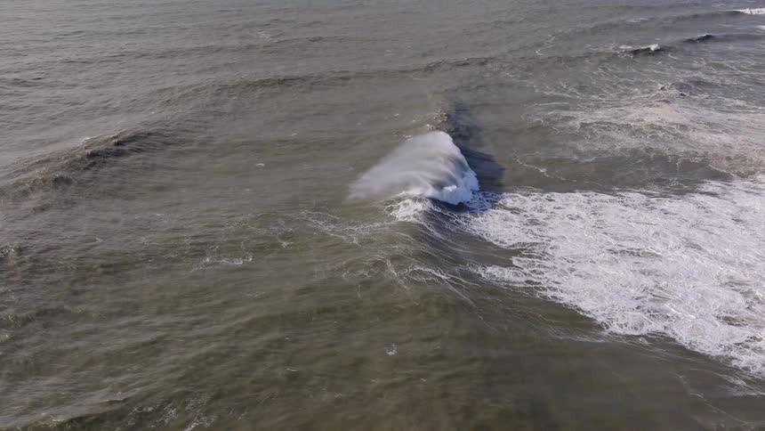 A dramatic slow-motion aerial view of a powerful ocean wave cresting and breaking in a stormy sea