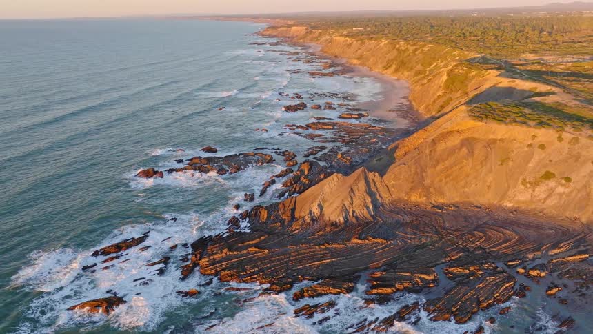 A majestic aerial view of a rugged coastline at sunset, with waves crashing against dramatic rock formations