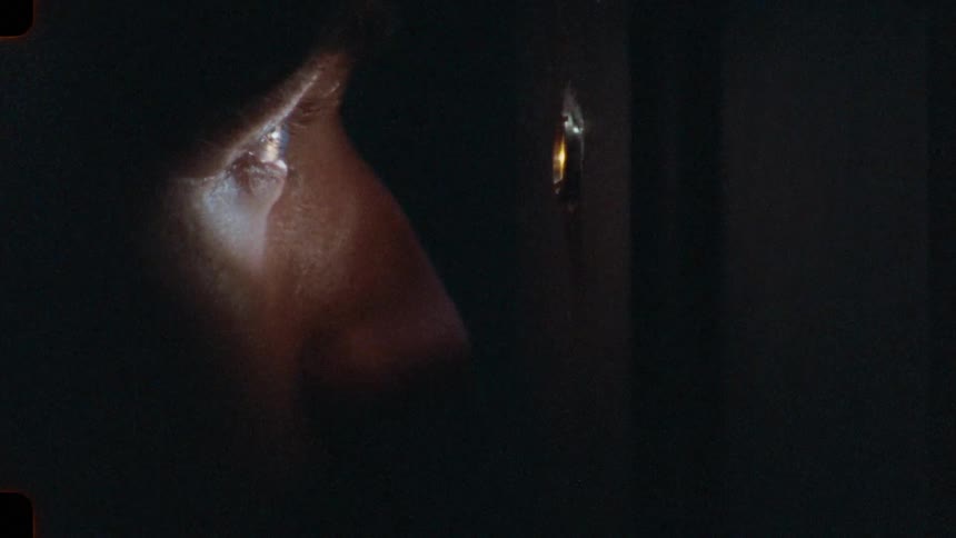 A cinematic close-up of a suspicious person's eye looking through a door peephole in a dark room