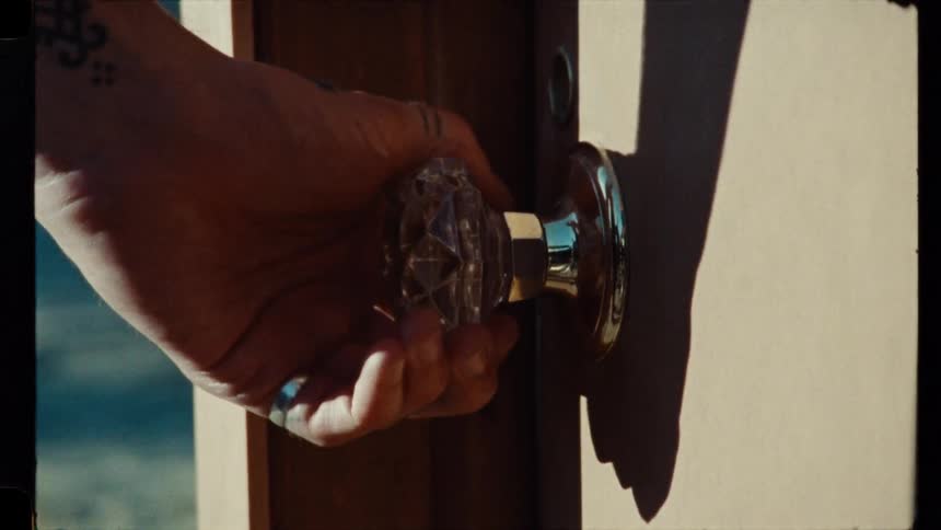 A hand with a tattoo and ring slowly turns a vintage crystal doorknob in this close-up, retro-style footage