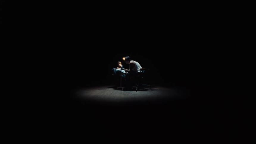 A tattoo artist meticulously works on a client's arm, illuminated by a single spotlight in an otherwise dark space