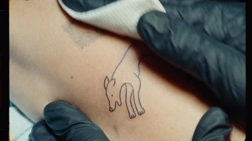A tattoo artist wearing black gloves carefully wipes away a temporary stencil from a new fox tattoo on a client's arm