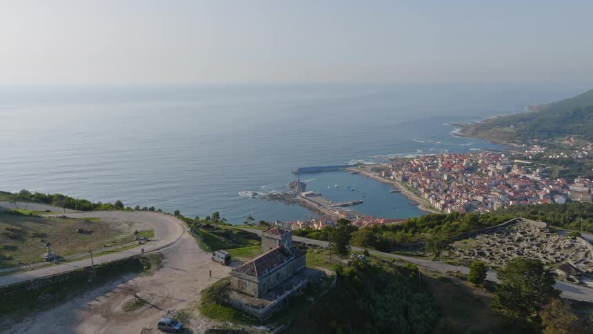 An expansive aerial view rises over a historic hilltop church to reveal the coastal town and harbor of A Guarda in Galicia, Spain, nestled by the Atlantic Ocean