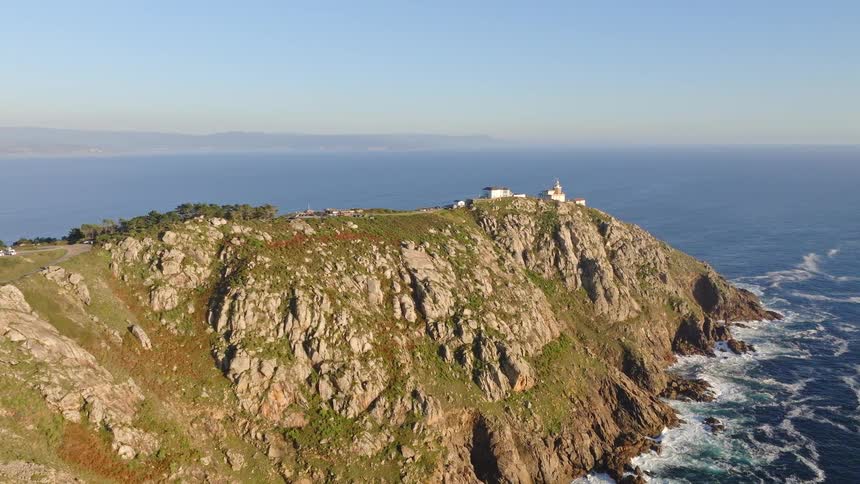 A stunning aerial view of a lighthouse perched atop a rugged, rocky cliff overlooking the vast blue ocean