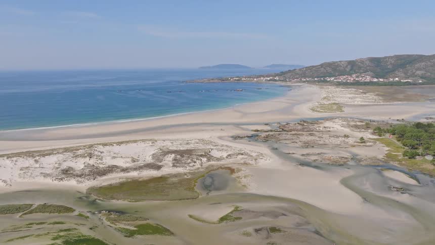 A sweeping aerial view reveals a vast coastal ecosystem where a white sand beach and tidal wetlands meet the beautiful blue ocean