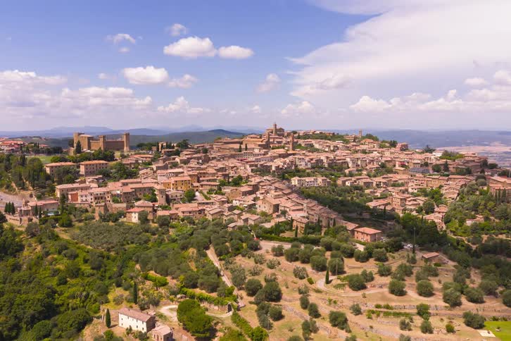 A beautiful aerial shot ascends over the historic hilltop town of Montalcino, nestled in the scenic green landscape of Tuscany, Italy