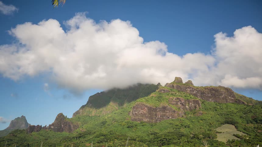 A time-lapse of fluffy white clouds drifting over a majestic green tropical mountain