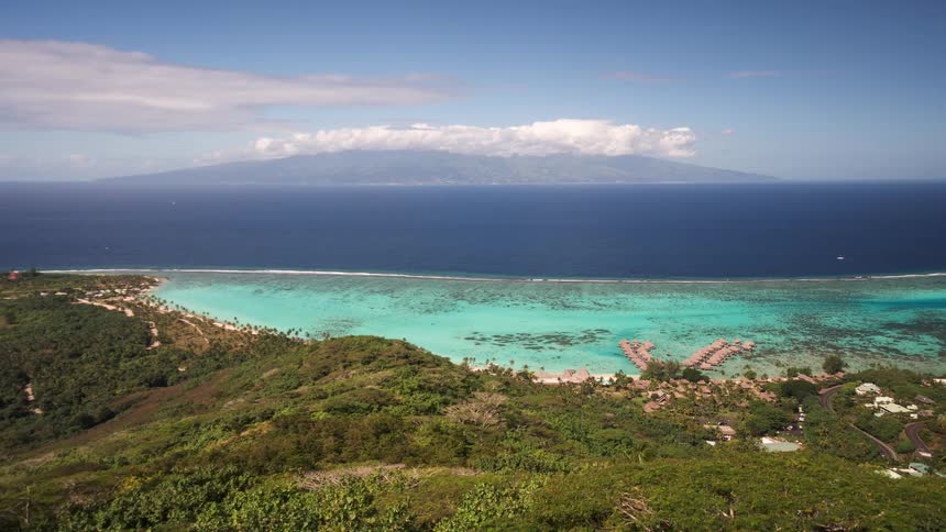 A stunning high-angle timelapse from a viewpoint on Moorea, looking over the turquoise lagoon and coral reef towards the island of Tahiti