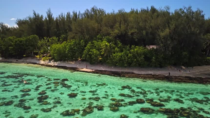 An aerial shot pulls away from a woman kayaking in crystal clear turquoise water to reveal a stunning tropical island landscape