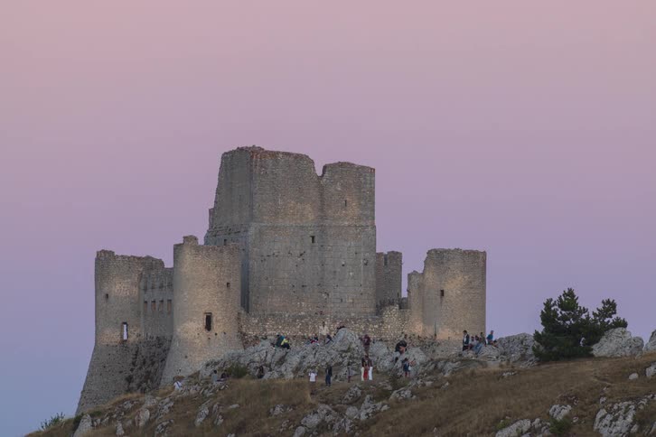 The ruins of the magnificent Rocca Calascio castle are filled with visitors enjoying the magical light of a pink and purple sunset