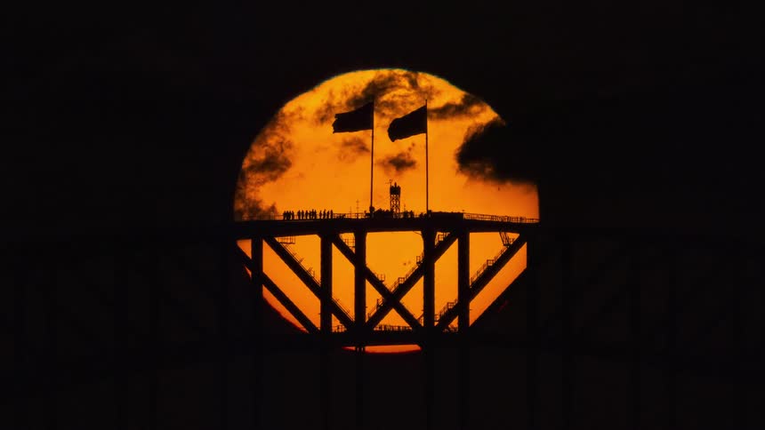 Dramatic time-lapse of the massive orange sun setting behind the iconic Sydney Harbour Bridge silhouette