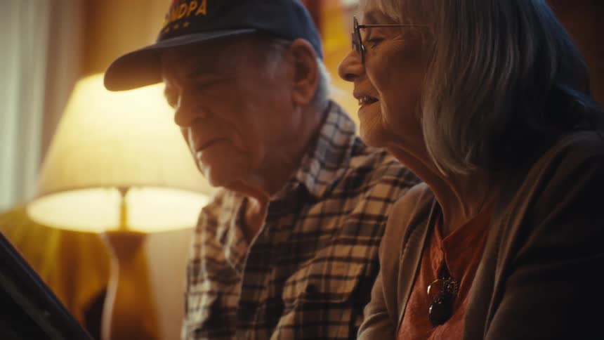 A senior couple fondly reminisces while looking through an old photo album together in their warmly lit home