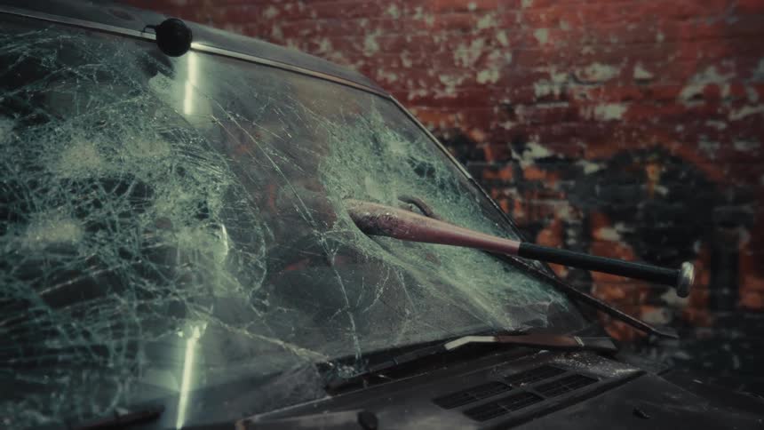 A dolly shot pulls back from a baseball bat lodged in the shattered windshield of a vandalized car