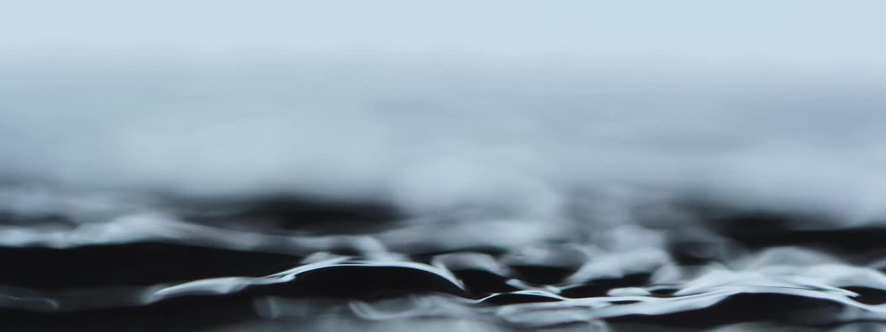 Hypnotic slow-motion ripples on the surface of a dark liquid create an abstract, calming visual