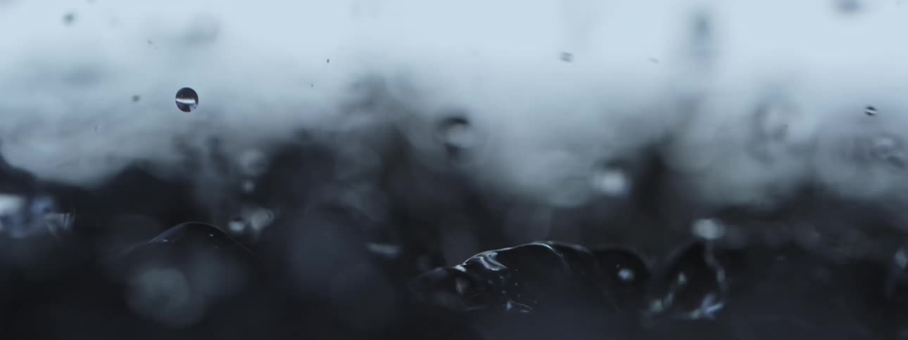 A moody, abstract macro shot captures water droplets splashing and dancing in slow motion