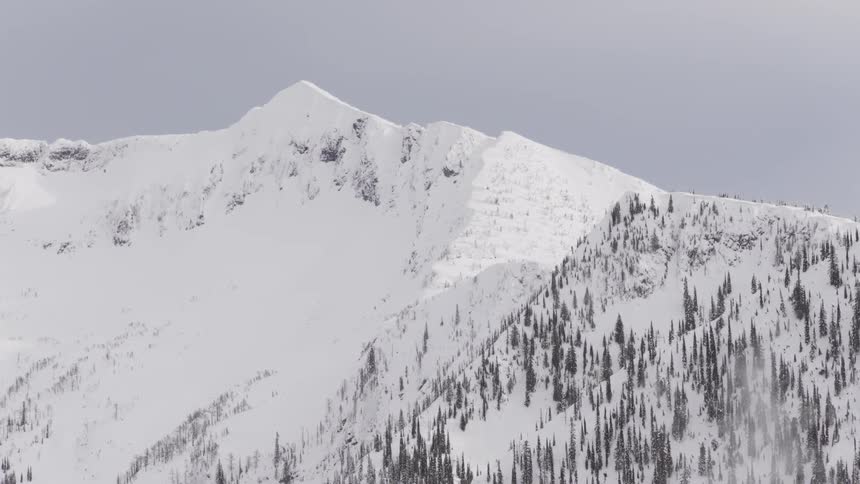 A beautiful and snowy mountain peak stands tall against a white, overcast sky in winter