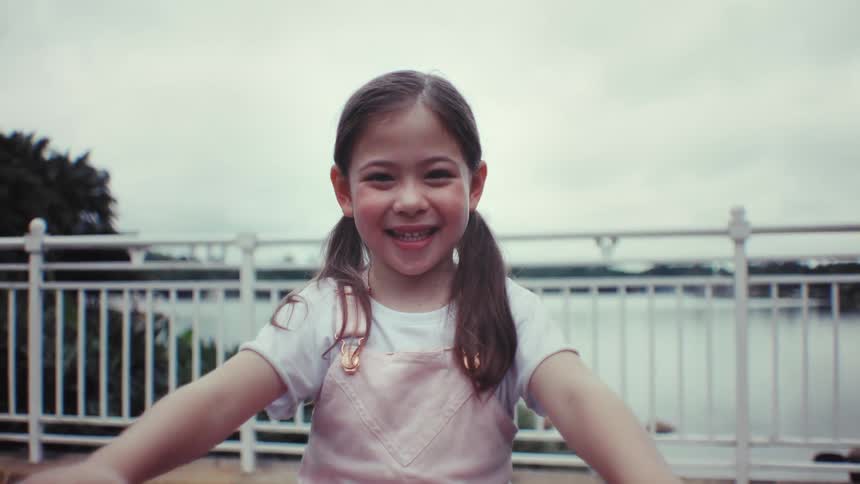 Portrait of a joyful young girl with pigtails smiling brightly in front of a lake