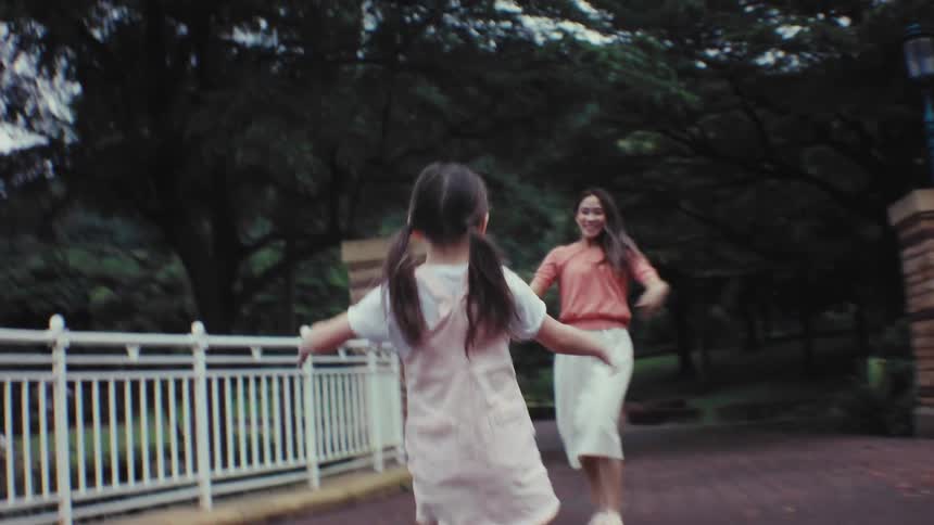 A happy little girl runs across a park bridge in slow motion and into her smiling mother's loving embrace