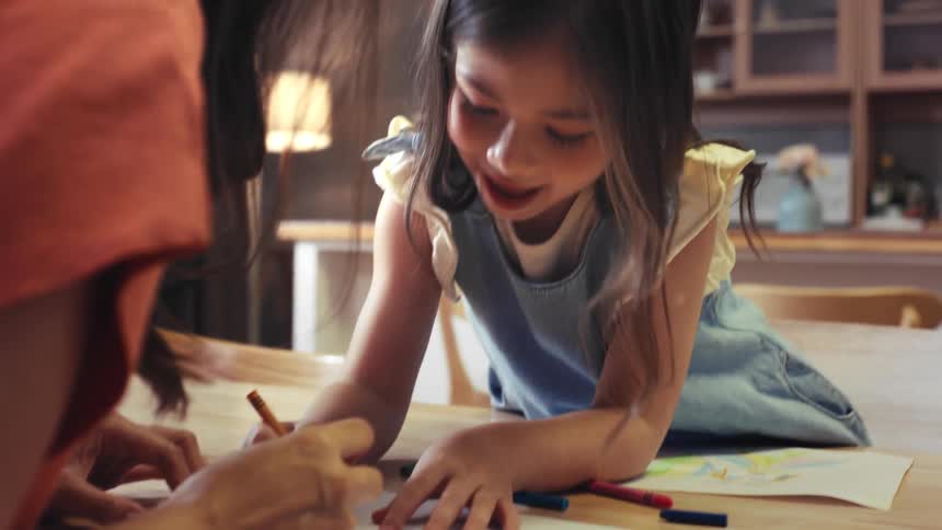 A loving mother and her happy young daughter spend quality time together drawing with crayons at their kitchen table