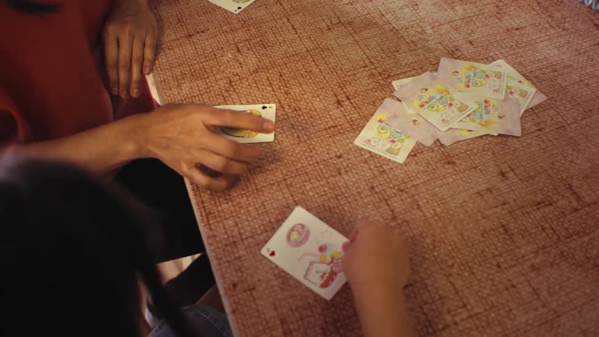 An over-the-shoulder view of a mother and child playing a fun cartoon card game at the kitchen table