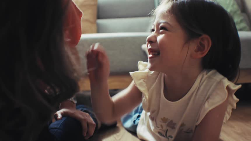 Happy young girl smiles lovingly at her mother while they read a storybook together on the living room floor