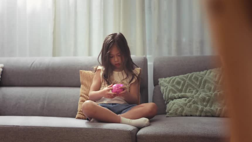 An adorable little girl sitting on the sofa joyfully celebrates a win while playing with a pink toy