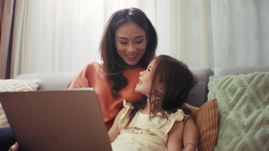 A heartwarming slow-motion shot shows a loving mother and her daughter sharing a happy moment while looking at a laptop at home
