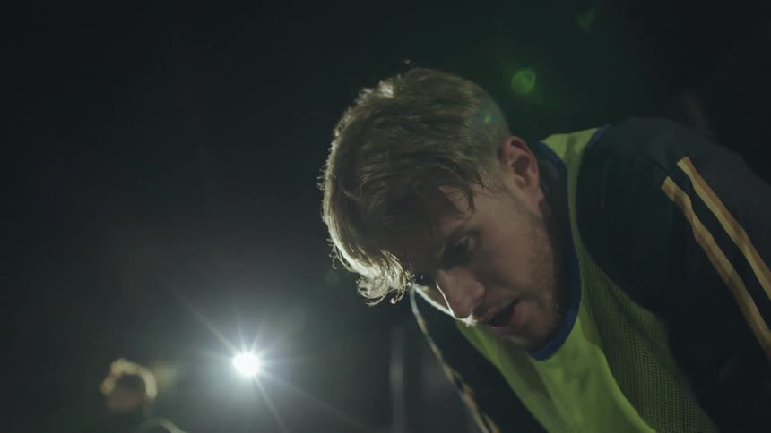 Close up of an exhausted soccer player catching his breath under bright stadium lights during a nighttime match