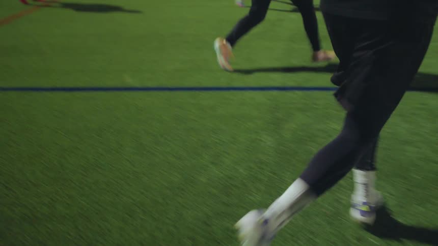 Dynamic slow-motion footage follows a soccer player from behind as he participates in a nighttime passing drill with his team