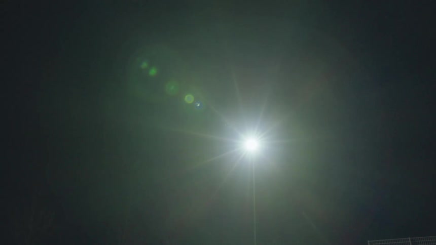 A bright light post shines with a large lens flare through the dense fog on a dark night