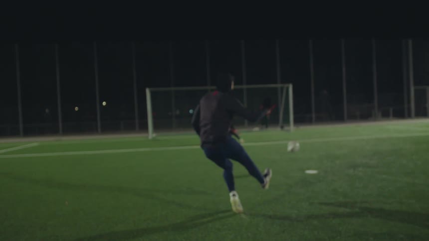 Slow motion shot of a soccer player dribbling down the pitch at night and taking a powerful kick towards the goal