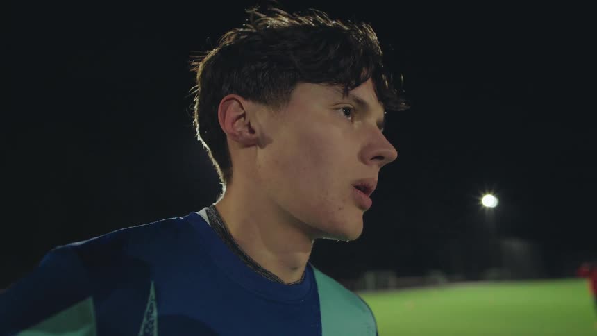 Close-up profile of a tired but determined male athlete catching his breath under stadium lights at night