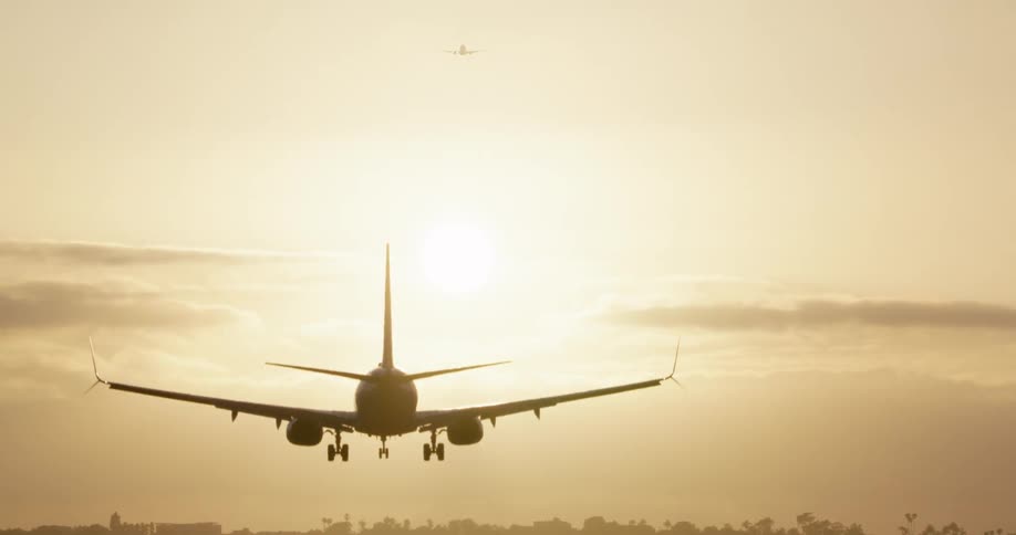 A passenger jet is silhouetted against a bright, hazy sun as it comes in for a landing