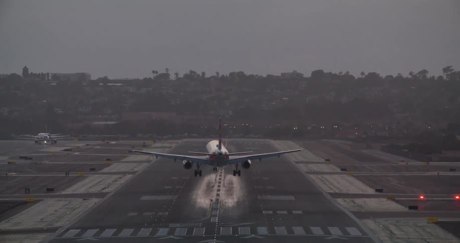 A commercial passenger jet makes a smooth landing on a runway at dusk, seen from a straight-on rear perspective
