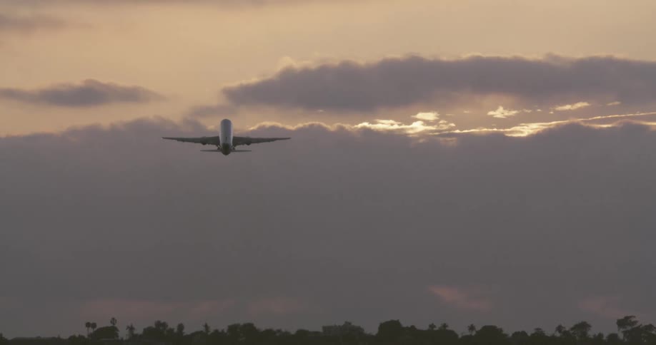 A passenger jet is silhouetted as it takes off and flies away into a dramatic sunset sky filled with clouds