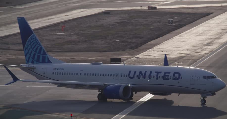 A United Airlines passenger jet taxis onto the runway at a busy airport, preparing for takeoff