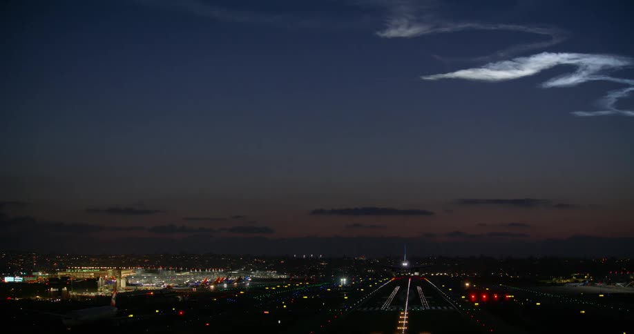 A passenger jet makes its final approach and lands on an illuminated runway at night