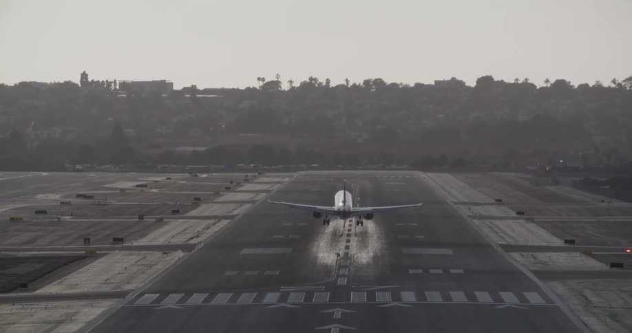 A passenger jet, seen from behind, glides down for a smooth landing on an airport runway before taxiing off
