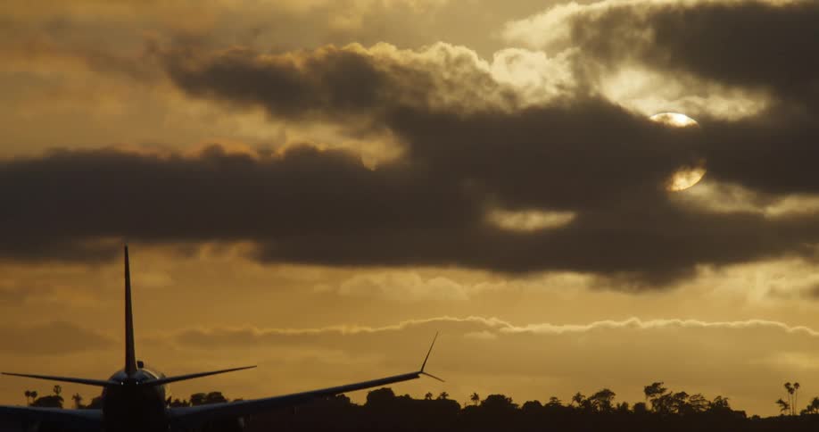 A silhouetted passenger airplane makes its final approach for landing against a dramatic golden sky at sunset