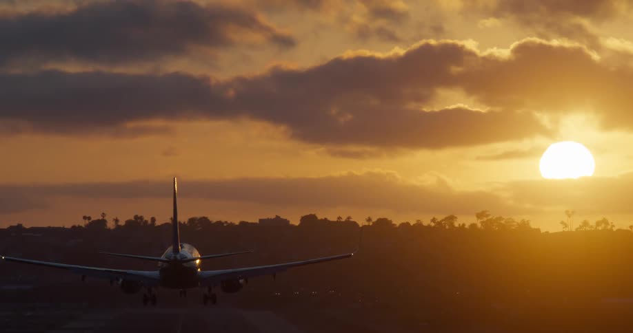Passenger airplane silhouette landing on an airport runway against a beautiful golden sunset
