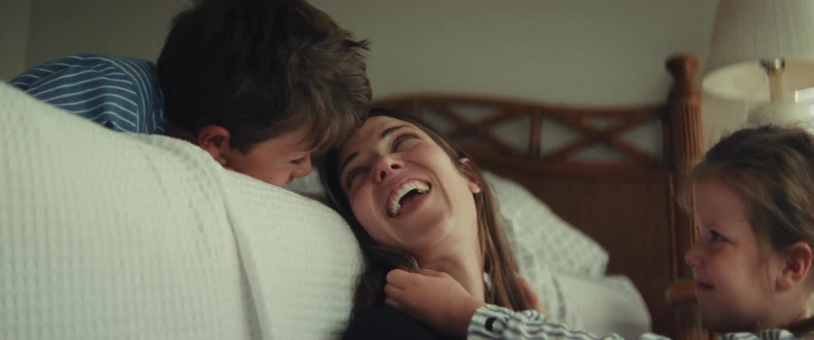 A mother shares a tender and playful moment with her two young children, a son and a daughter, in their bedroom