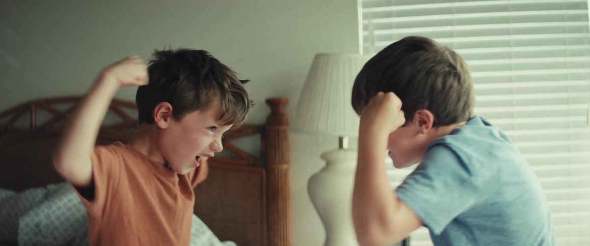 Two young brothers energetically play-fight in their bedroom in slow motion