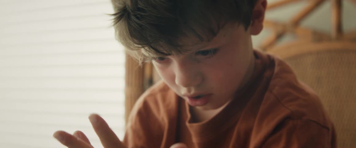 A focused young boy is seen in an intimate close-up as he concentrates on something off-screen, possibly learning or playing a game