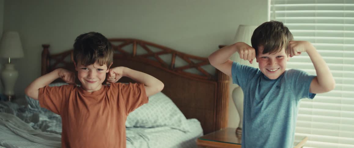 Two strong little boys happily show off their muscles while flexing in their bedroom